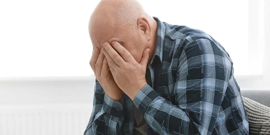 Elderly man covering his face with his hands.